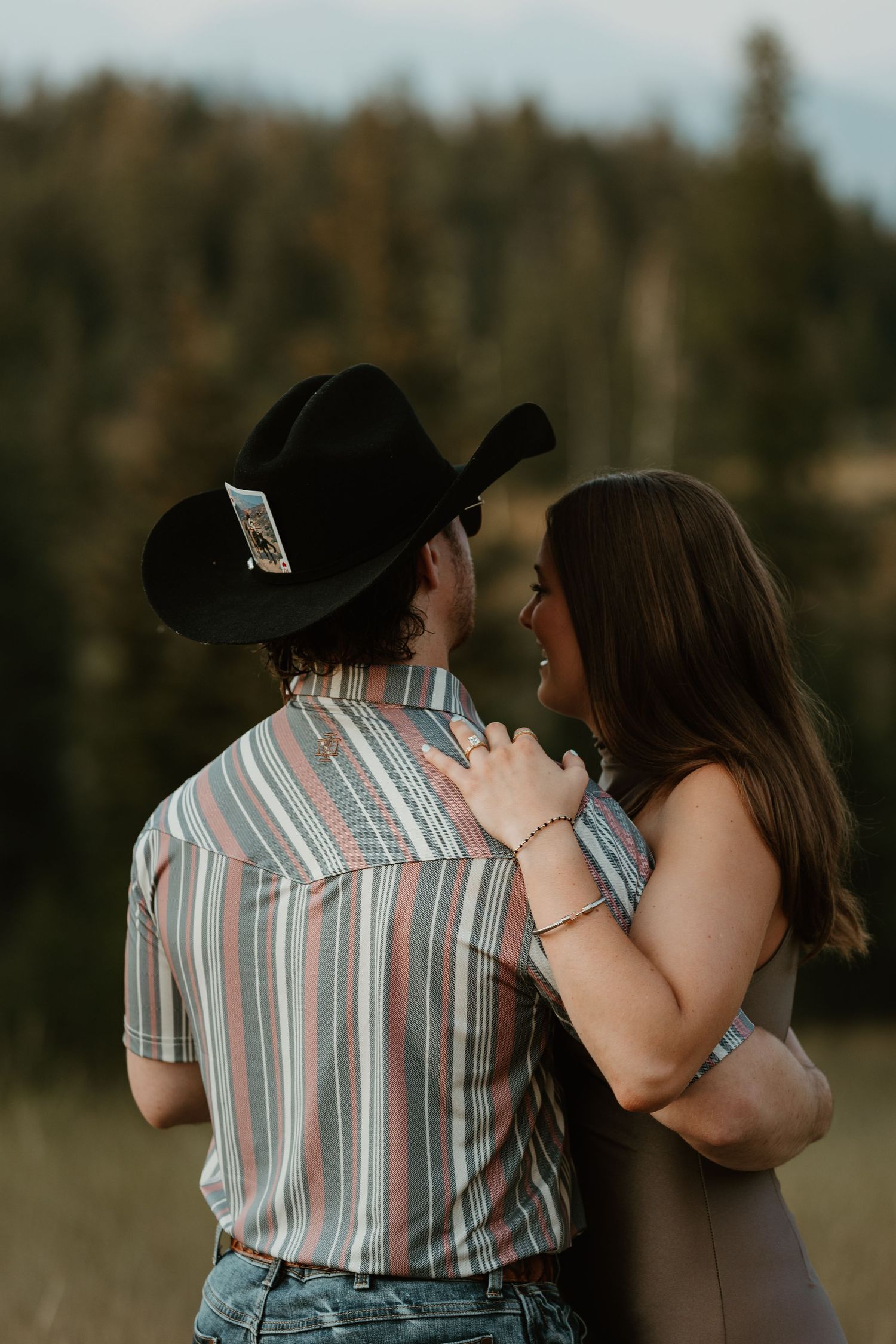 A couple in western attire share an intimate moment outdoors during golden hour.