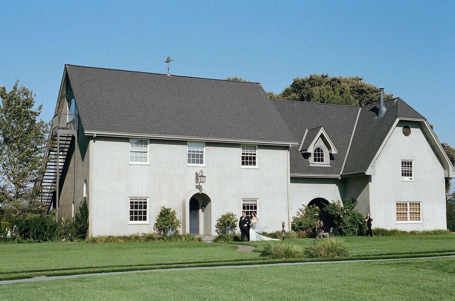A series of white residential houses with gray roofs sit along a grassy hillside on a sunny day.