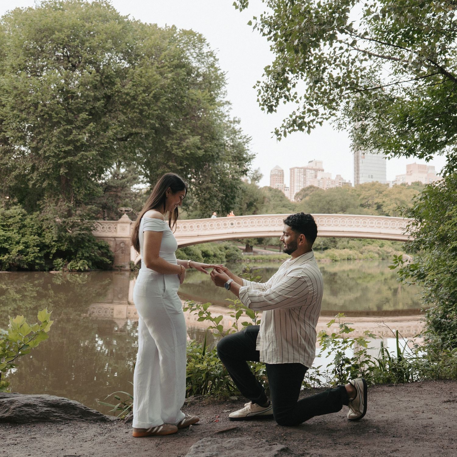 Sequence of a surprise marriage proposal by the river with trees and bridge in background.