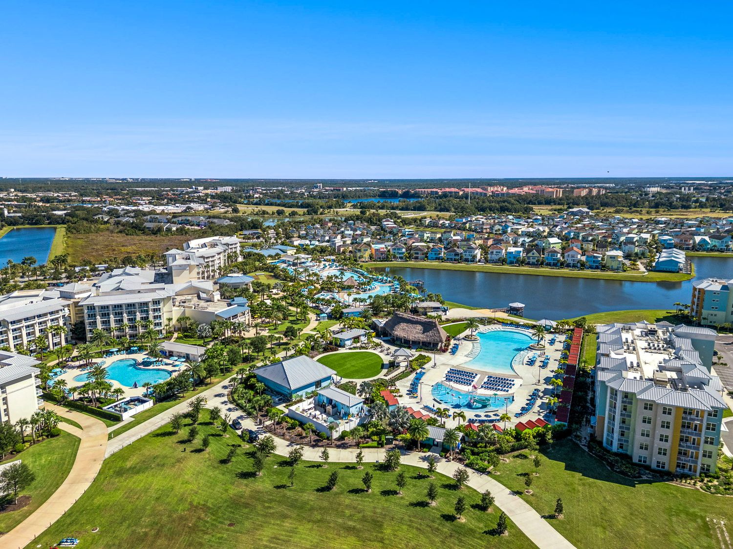 Aerial panoramic view of luxury waterfront resort community with pools, marina, and condominiums along Florida coastline.