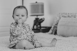 photo of an adorable baby sitting on a bed in a floral outfit, sucking fingers. | Motherhood + Family Photographer Westminster, CO