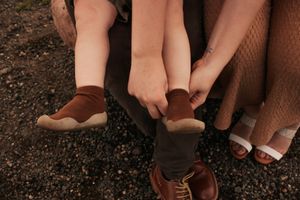 Close-up of adult hands helping a child put on brown socks and shoes,| Motherhood + Family Photographer Westminster,Co