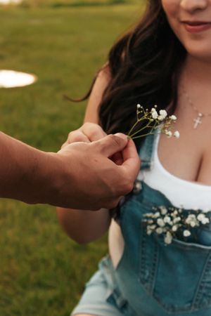 A man hands small white baby's breath flowers to a woman in denim overalls+ cross necklace | Motherhood + Family Photographer Westminster,Co