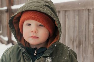 A child wearing a brown winter hat, warm clothing while snow falls on a winter day. |  | Motherhood + Family Photographer Westminster, CO
