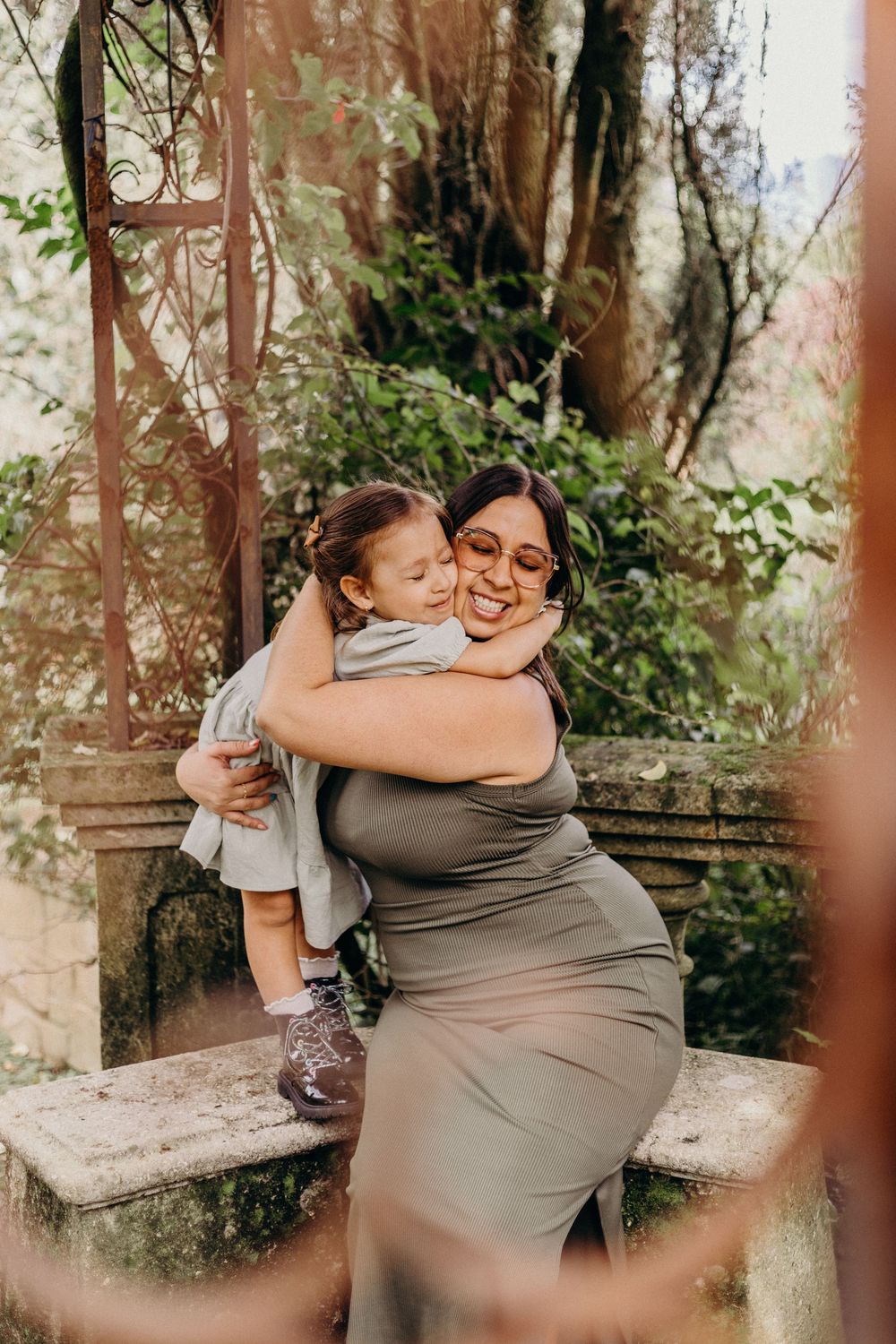 Candid outdoor portrait showing a tender embrace between parent and child in a natural garden setting.
