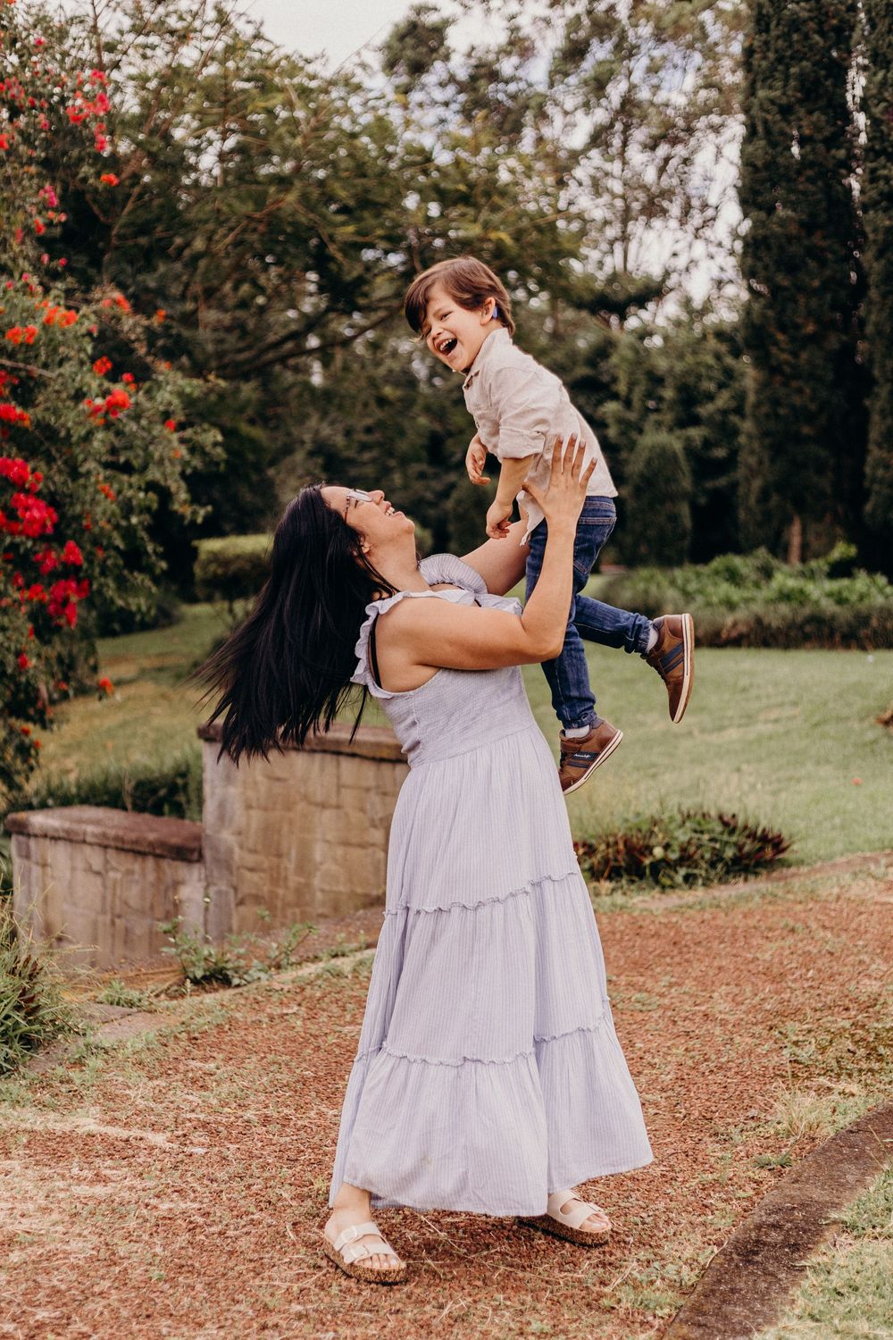 A joyful moment captured in a garden setting with a white tiered maxi dress and blooming red flowers in the background.