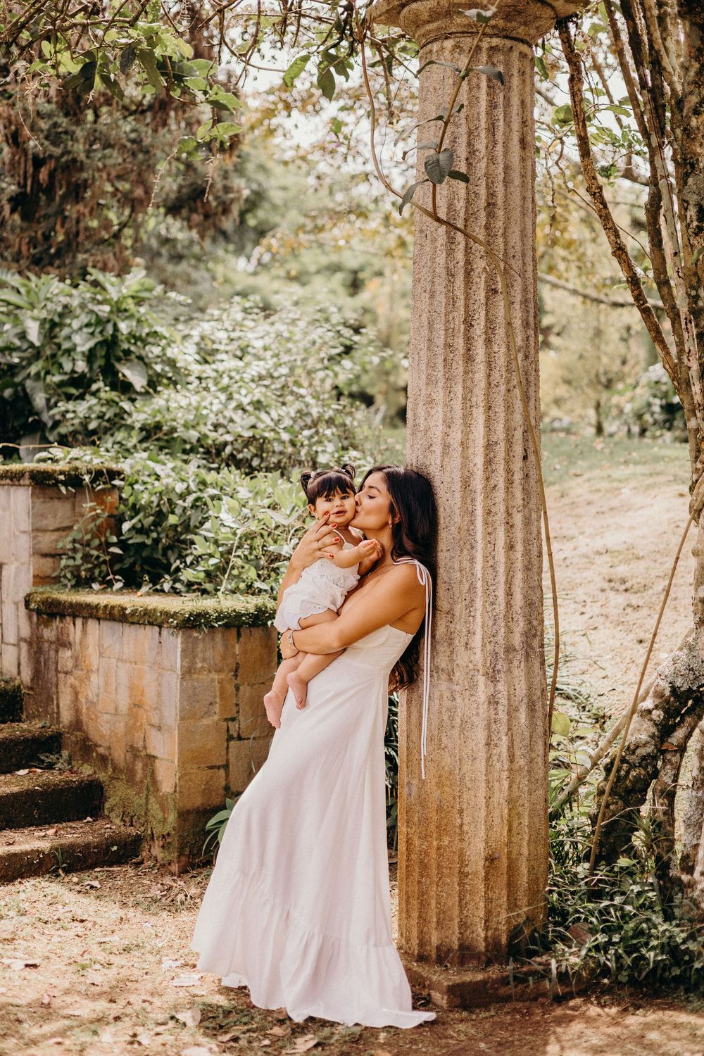 A romantic photoshoot among ancient stone columns in a garden setting with soft natural lighting.