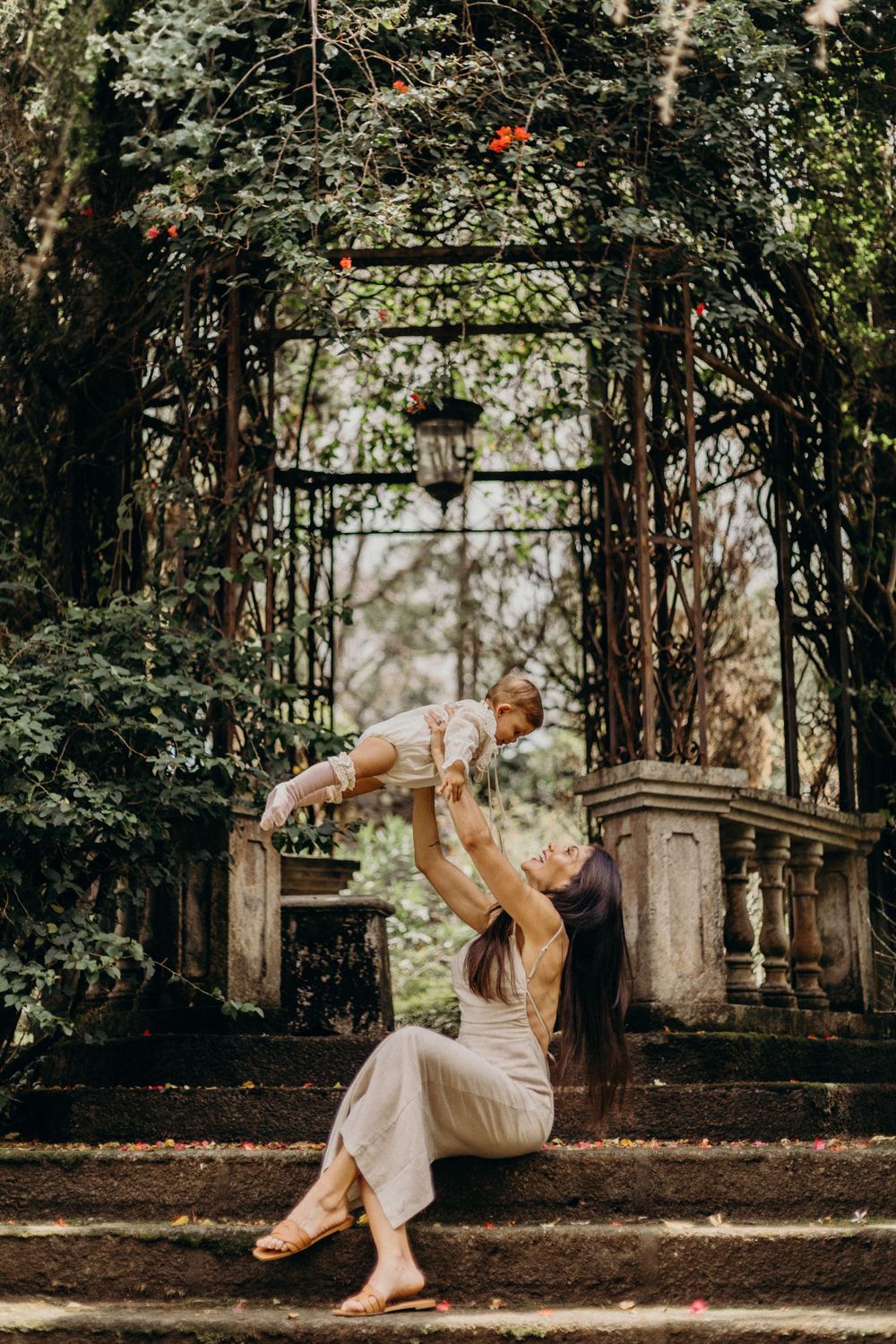 A couple shares a tender moment in a garden setting with natural lighting and lush greenery in the background.