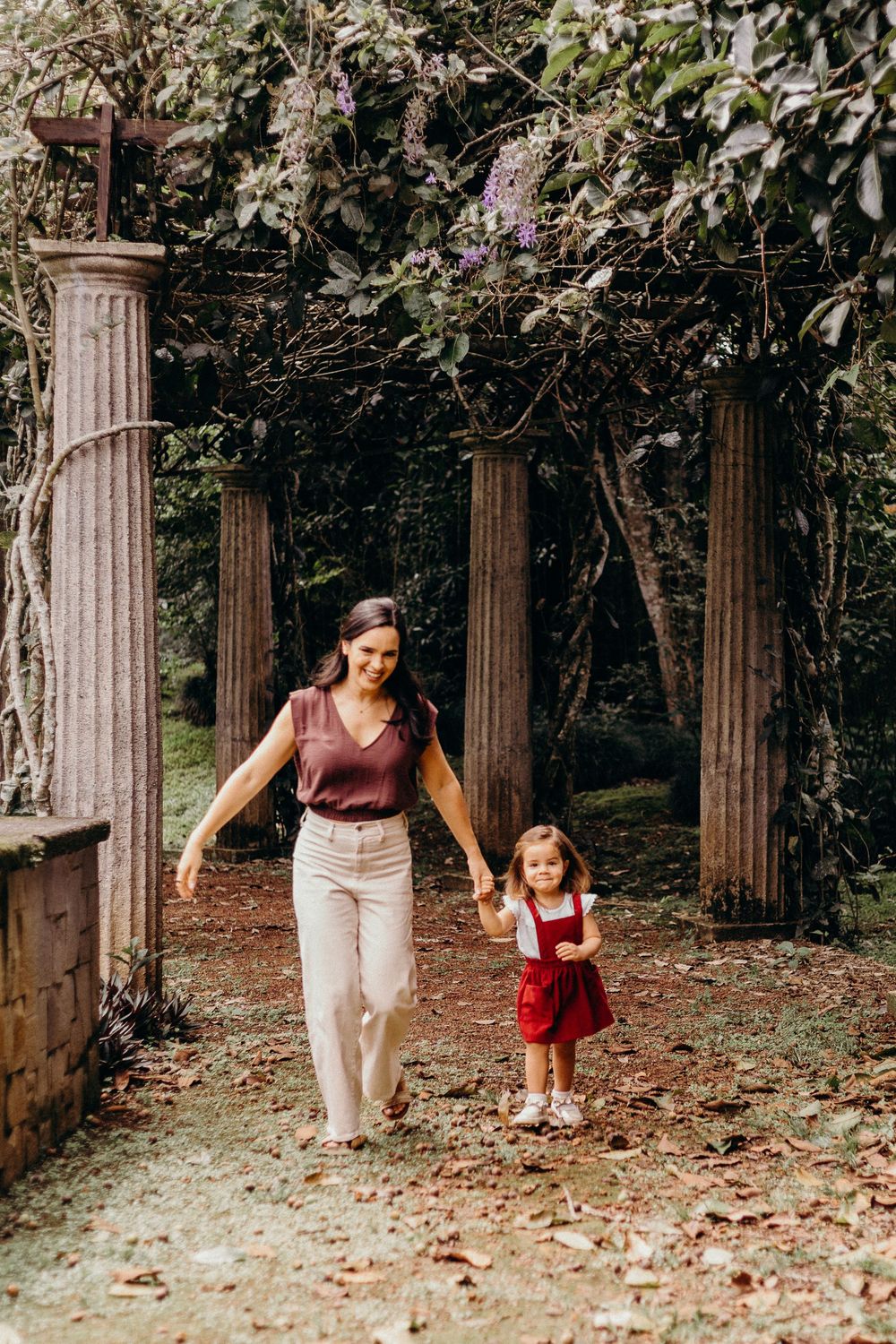 A series of candid photos showing a mother and child walking and playing among stone columns in a wooded garden setting.