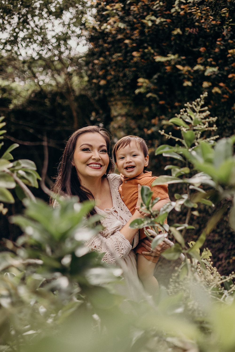 Two people share a joyful moment together while surrounded by lush green foliage in an outdoor setting.