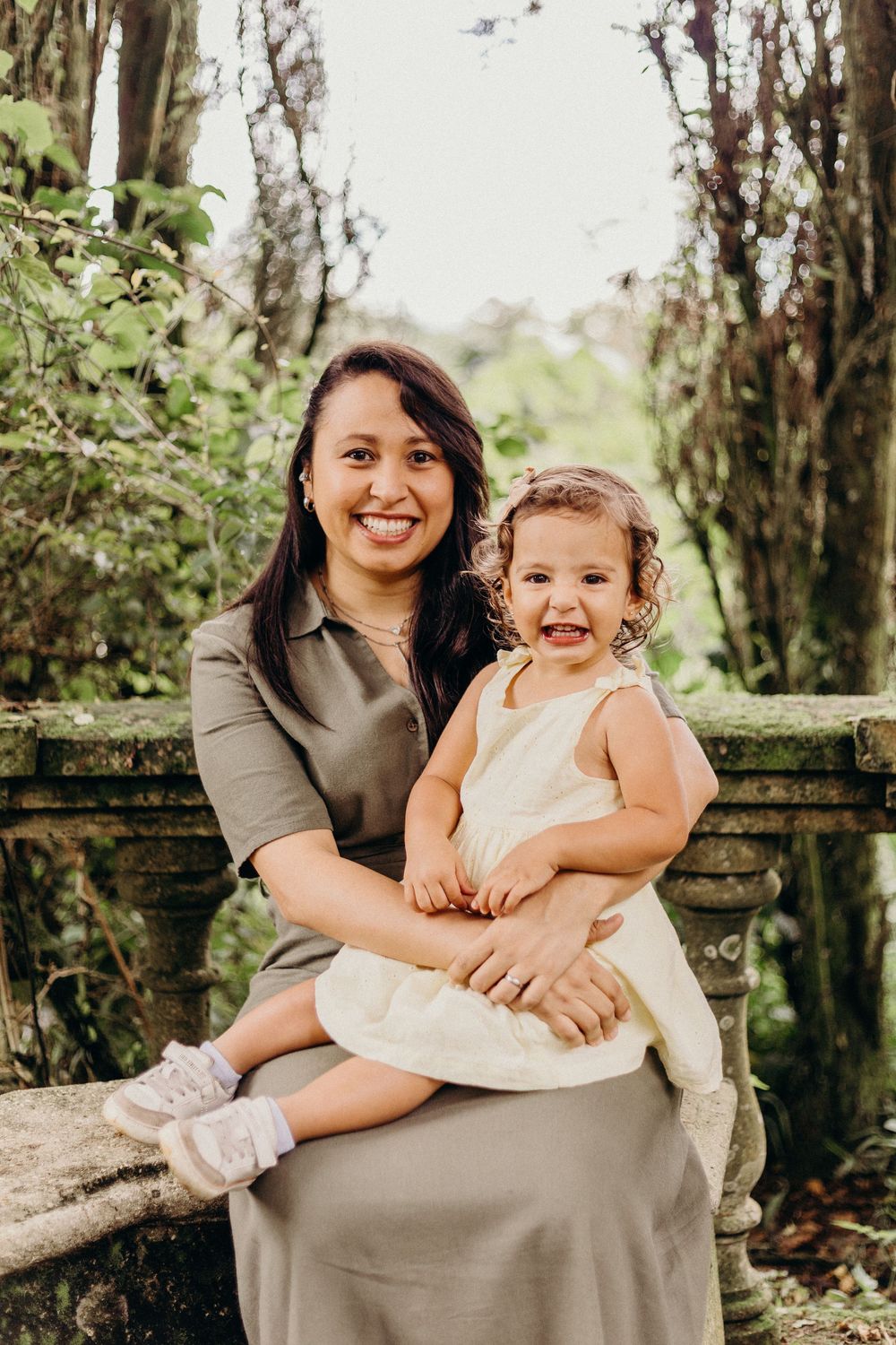 A parent and child share joyful moments while sitting on a stone bench in a wooded outdoor setting.