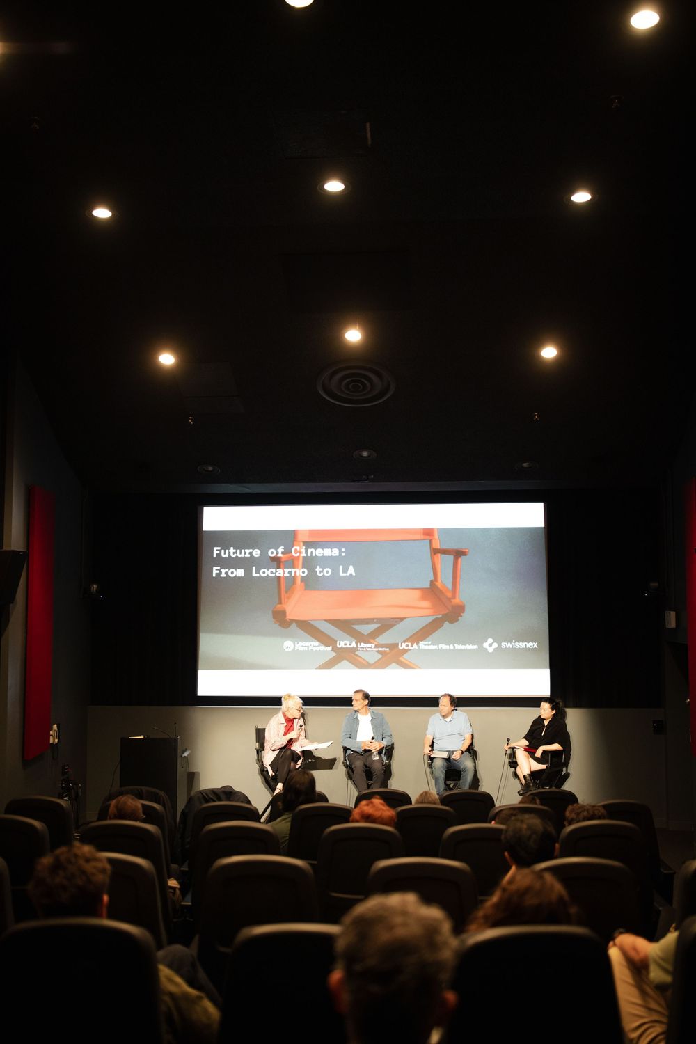 Panel discussion at Future of Cinema: From Locarno to LA event, with four speakers seated on stage in a screening room.
