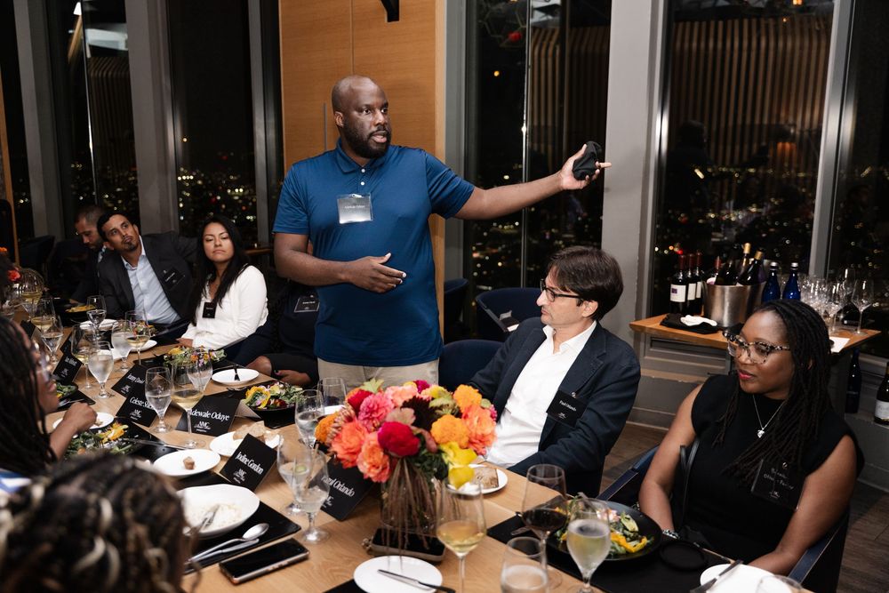 Man speaking at an elegant dinner event, gesturing while seated guests listen attentively at a decorated table.