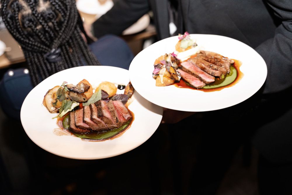Grilled steak slices arranged on white plates with garnish and sauce, showcasing fine dining presentation.