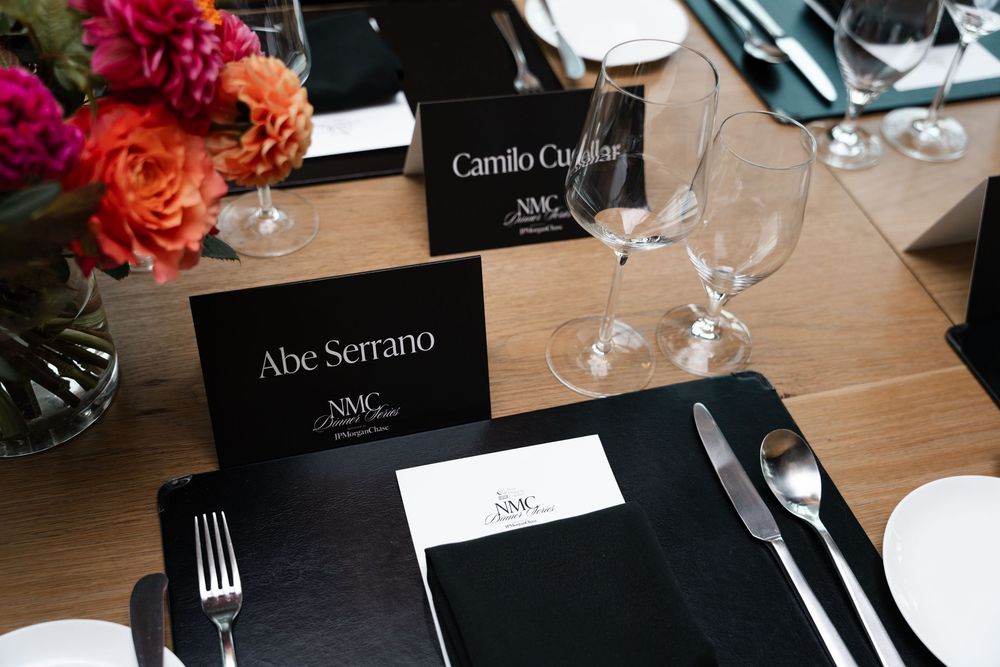 Black and white place cards with elegant typography sit alongside polished silverware at an upscale dining table setting.