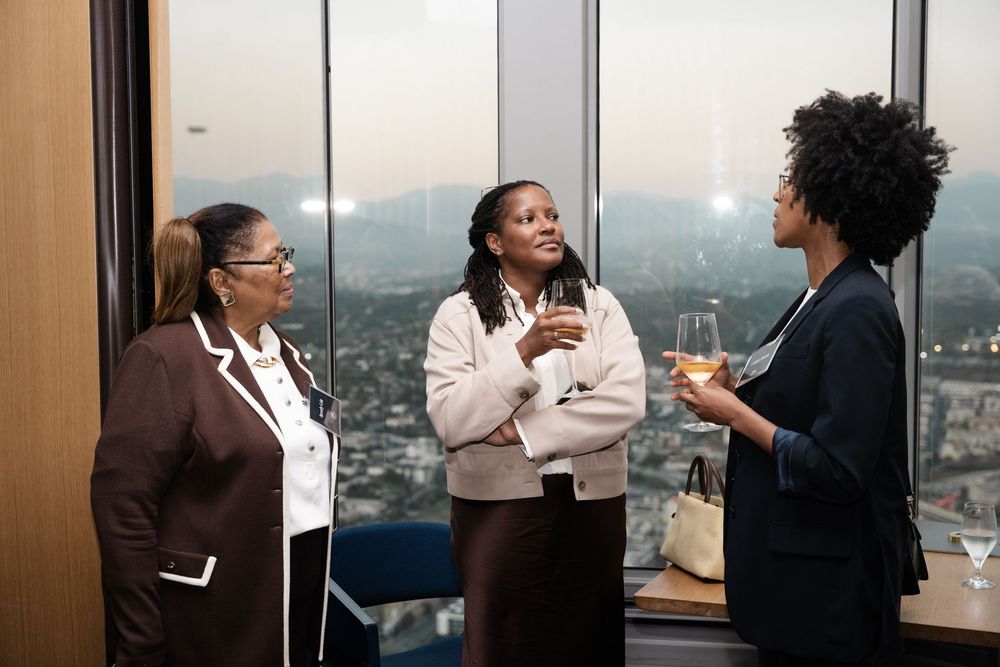 Three professionals having an animated business conversation in a modern office with city views through the windows.
