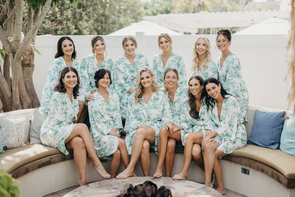 Bridesmaids wearing matching mint green floral robes sit together during wedding preparations.