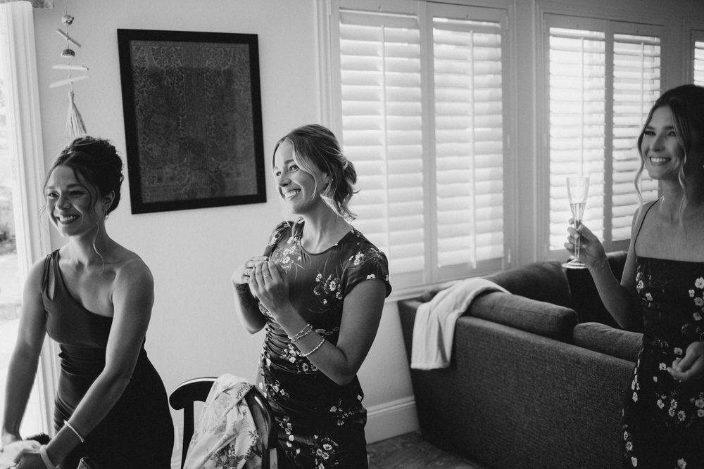 Black and white photo of wedding party preparations in bright room with shuttered windows.