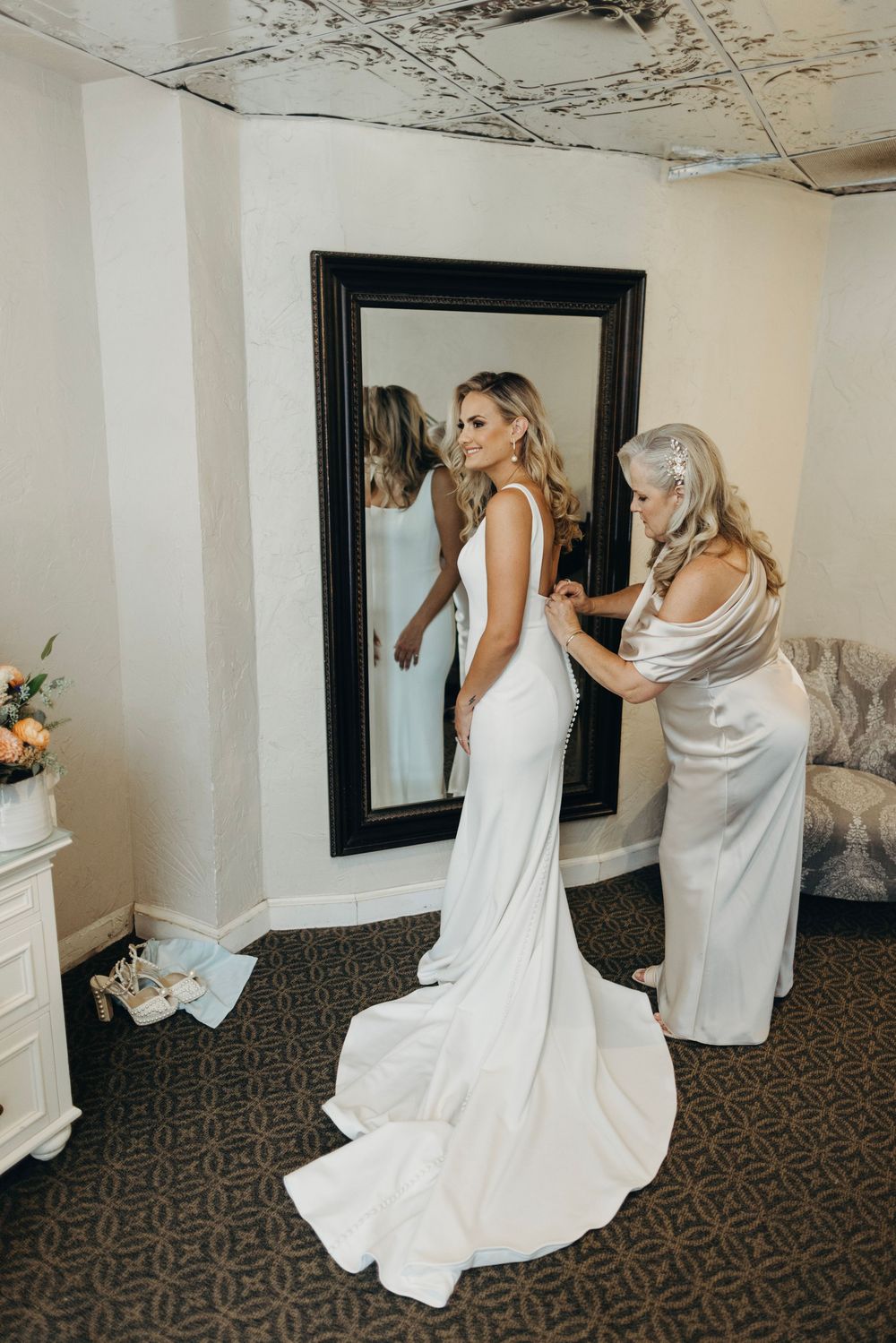 Wedding dress fitting and adjustments in elegant room with patterned carpet.