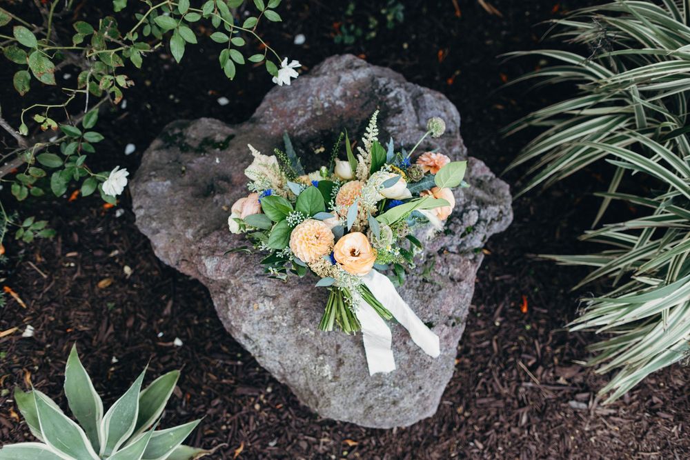 Wedding bouquets with peach and white flowers placed on natural stone garden accents.