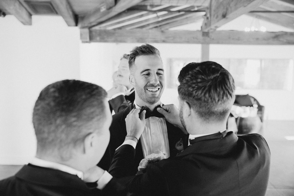 Wedding party members help each other get ready in a bright indoor space.