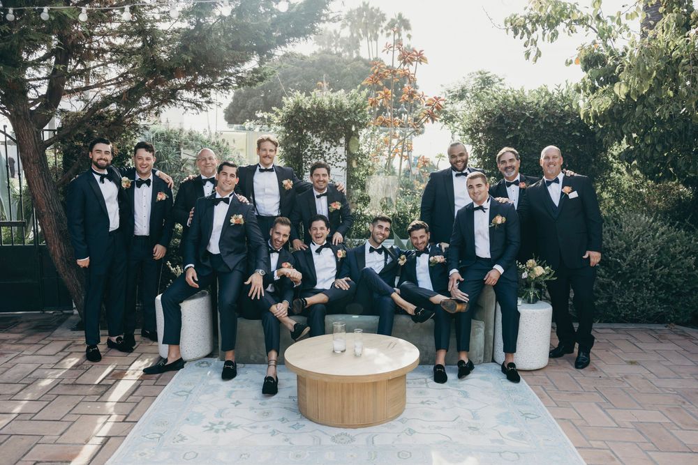 Wedding party members in formal attire gather around a table outdoors.