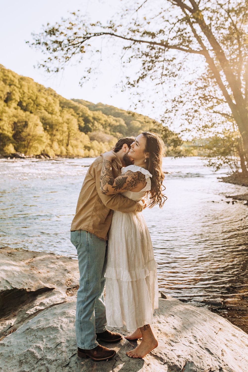 Couple kissing by a scenic river, woman in white dress, man in tan shirt.