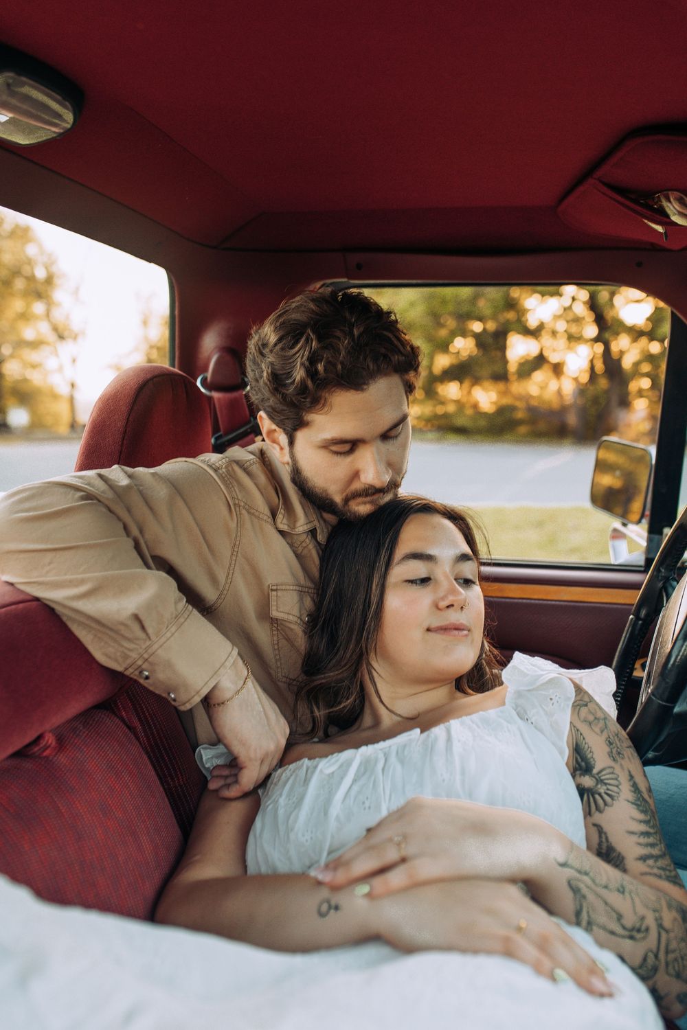 A couple relaxes inside a vintage red truck, the woman lying back with closed eyes as the man holds her gently.
