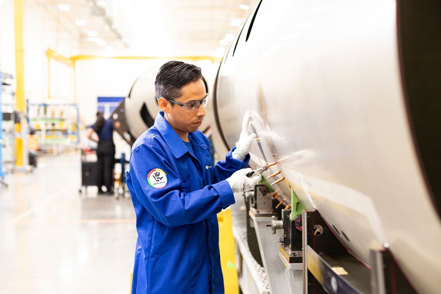 Manufacturing worker in blue uniform inspects aerospace components in a modern factory facility.