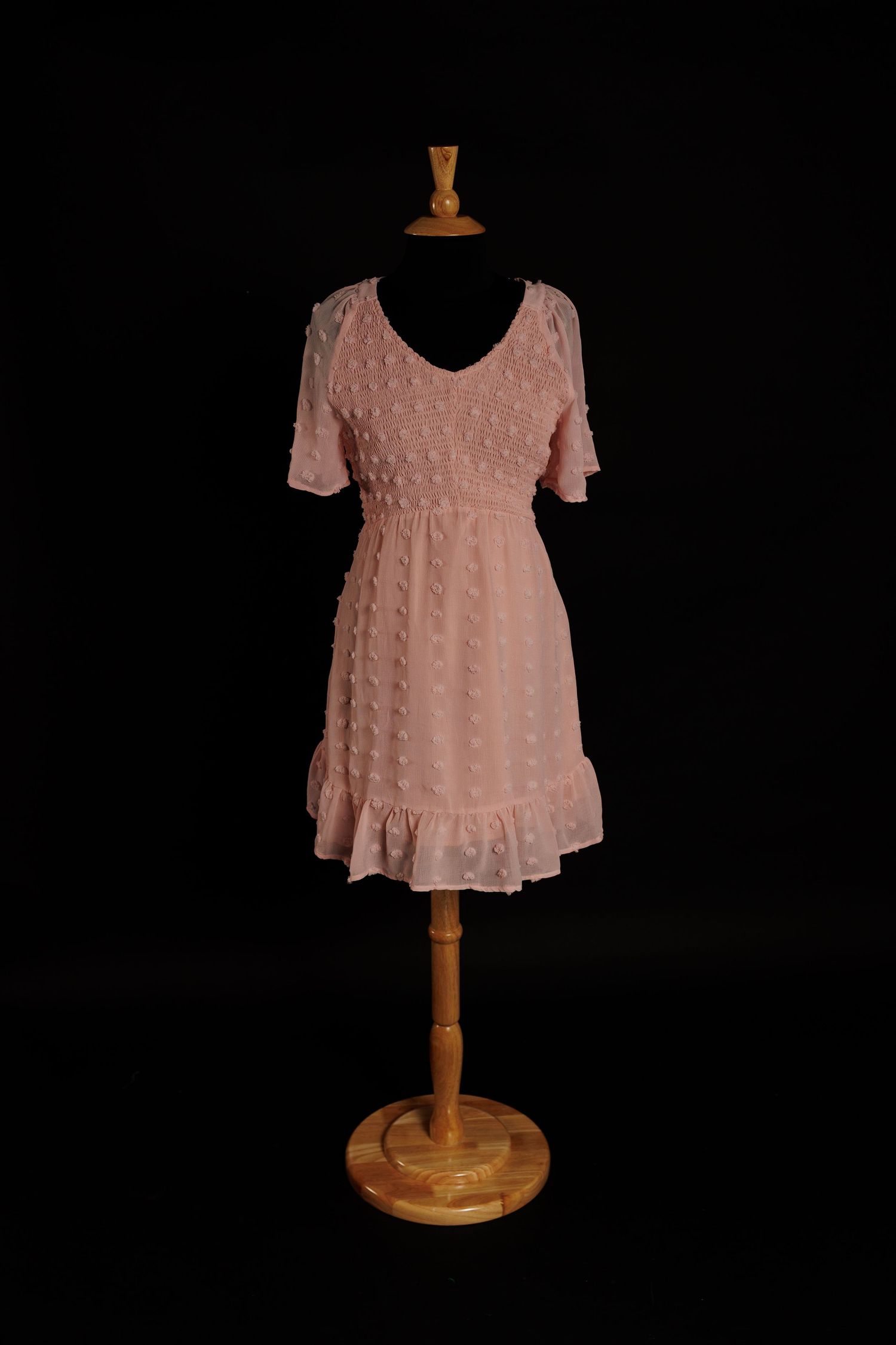 Blush pink Swiss dot maternity mini dress with flutter sleeves and ruffled hem on mannequin