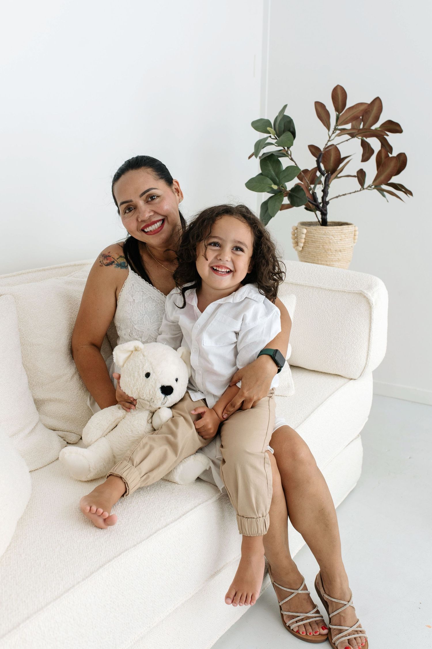 A parent and child share joyful moments together on a white couch with a plush teddy bear.