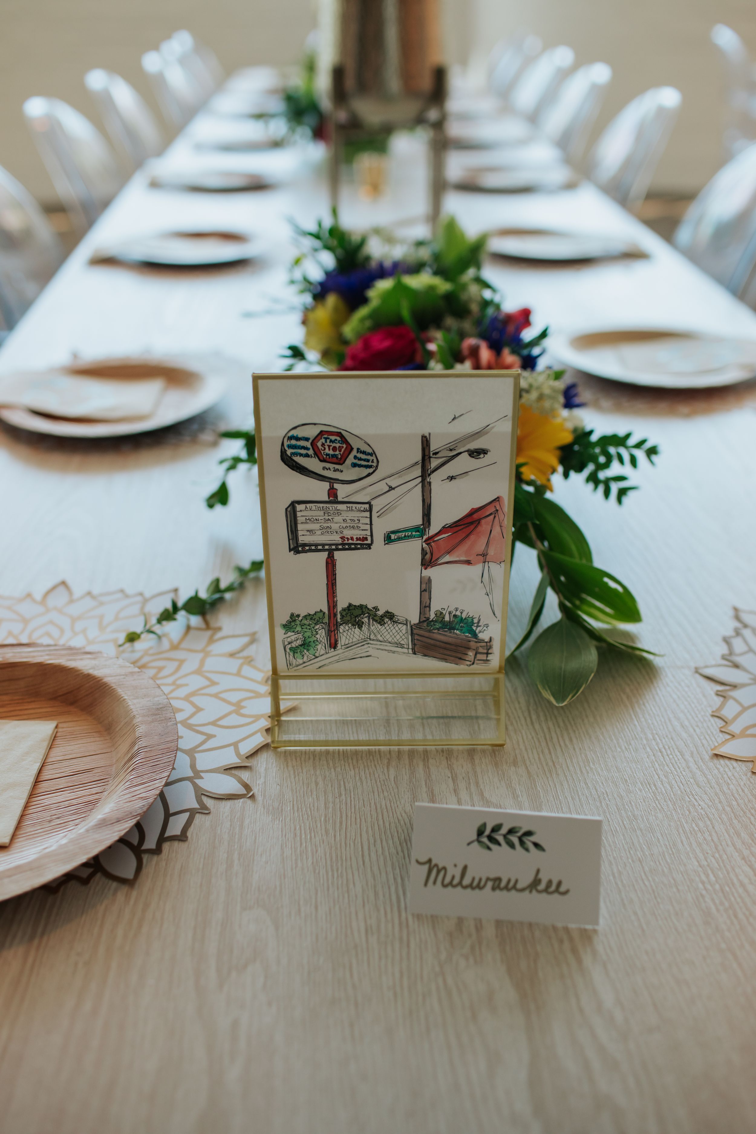 Illustrated place cards and floral centerpieces decorate an elegant table setting at a wedding reception.