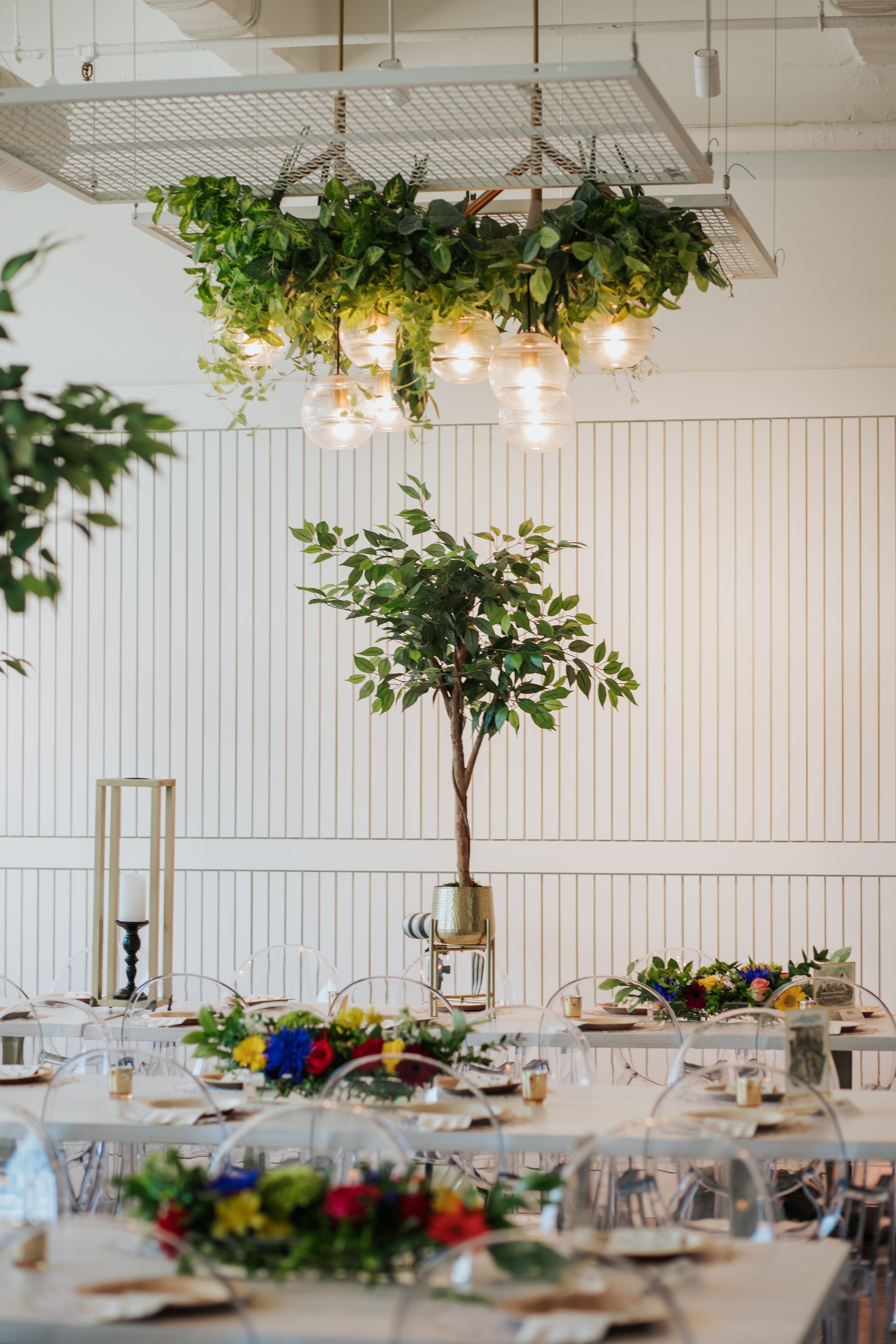 Modern white reception venue with hanging greenery, pendant lights, and table settings for a wedding celebration.