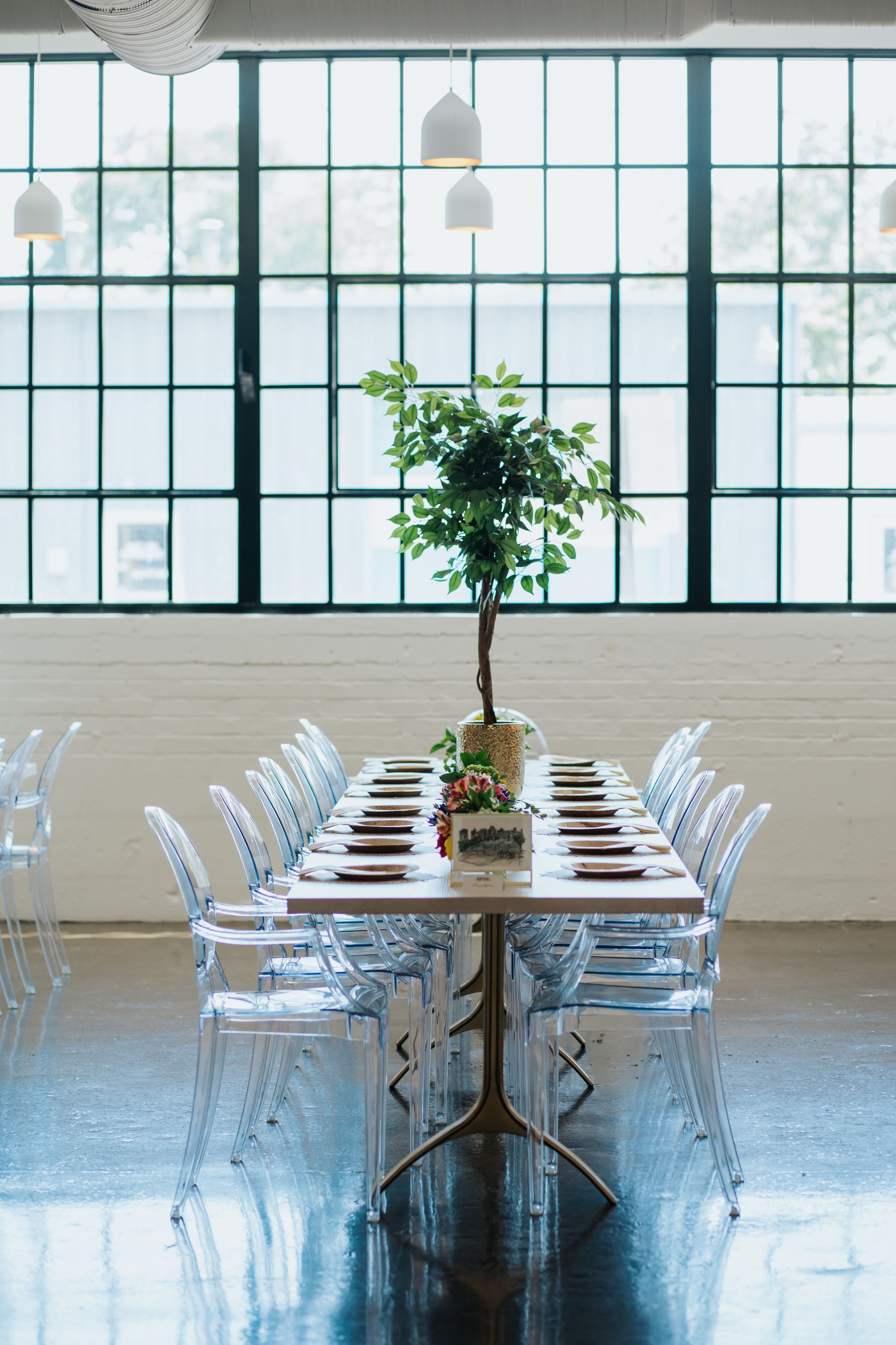 Industrial chic dining space with long tables, white chairs, and large windows creating natural light.