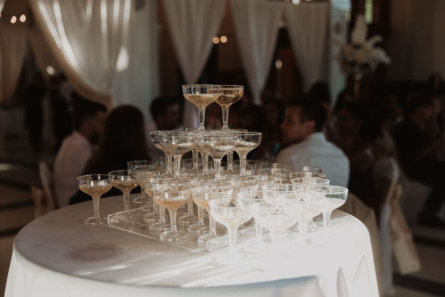 Elegant champagne tower with coupe glasses arranged on a white tablecloth at a wedding reception.