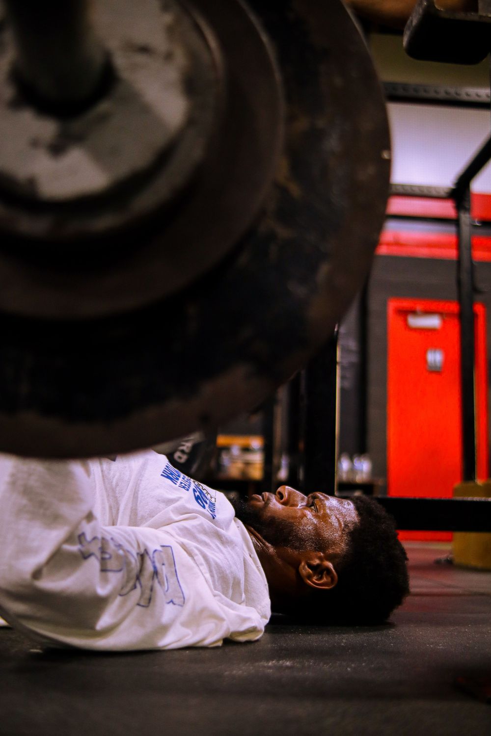 A mechanic lying on the floor beneath a vehicle, wearing a white uniform, working on repairs in an auto shop.