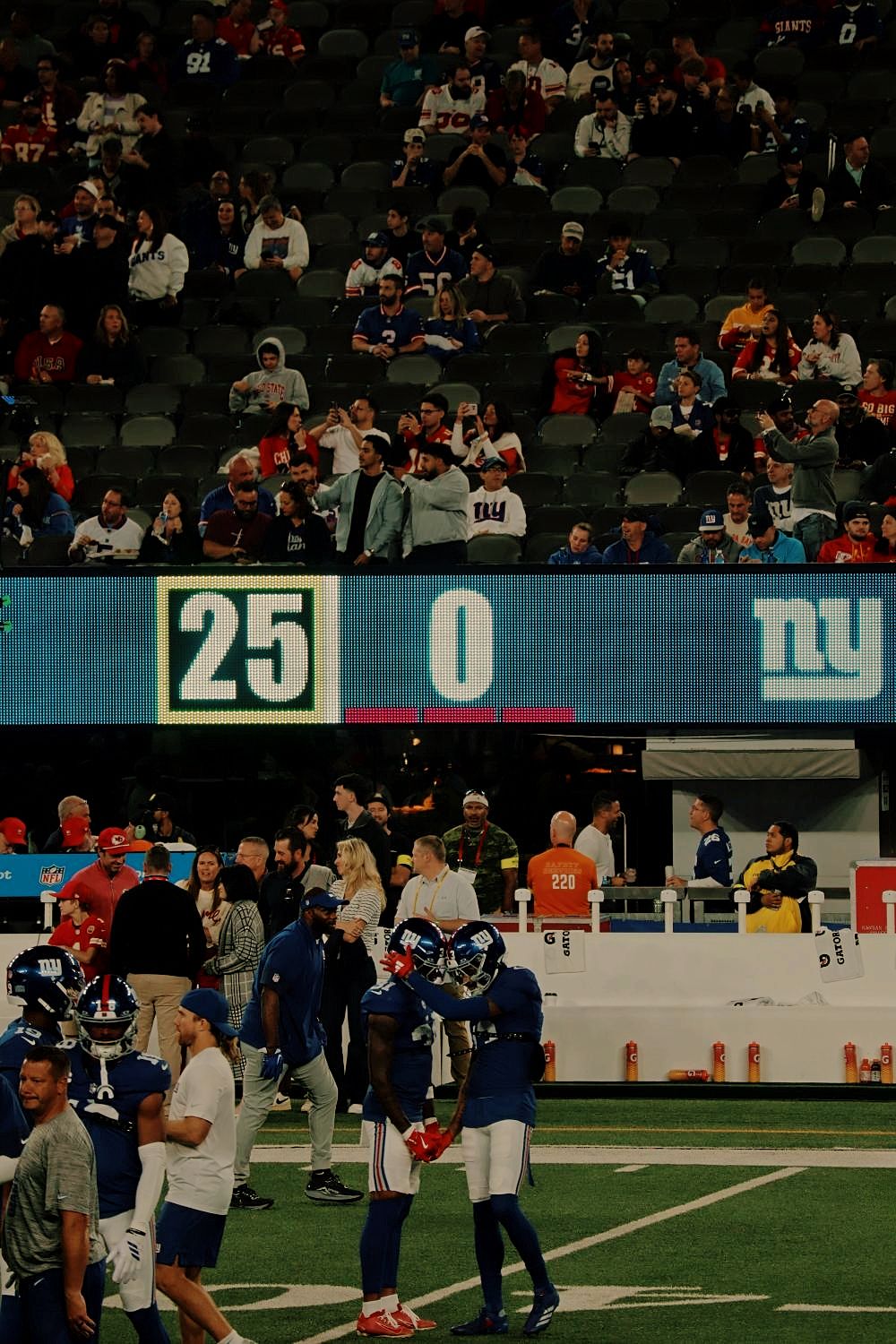 Football fans watch from stadium seats as players gather on the field during an NFL game with a scoreboard showing 25-0.