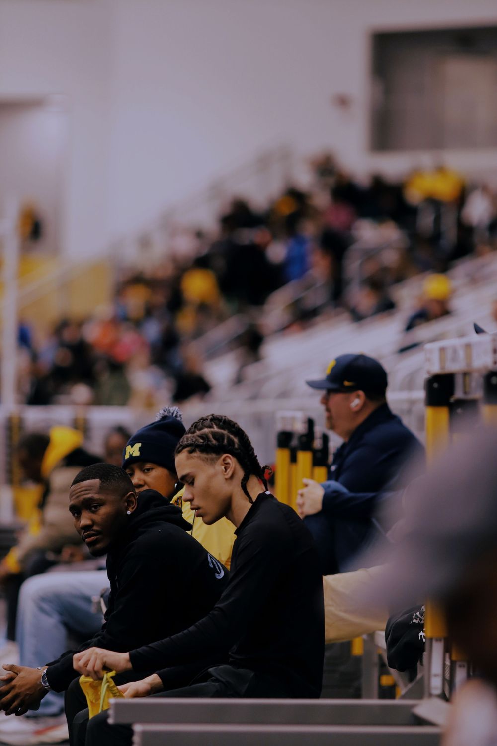 Sports fans in black jackets watch intently from stadium seats during a sporting event.