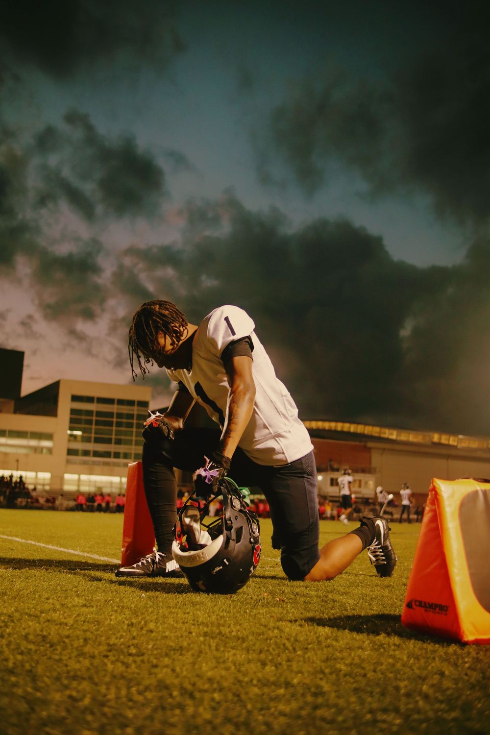 A person sits on grass near orange safety cones at dusk with a dramatic stormy sky overhead.