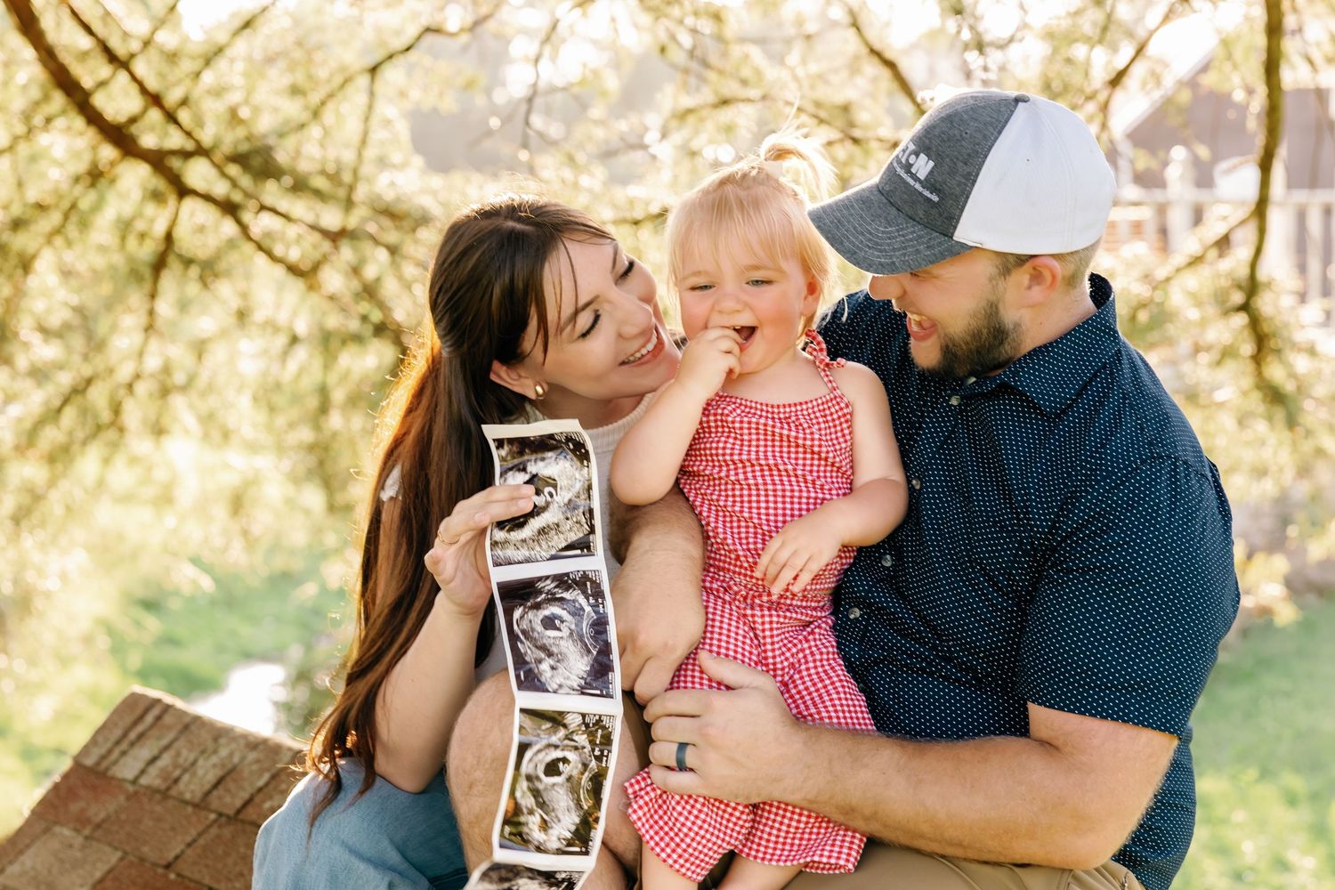 Family sharing special moment while holding ultrasound photo in sunlit outdoor setting.