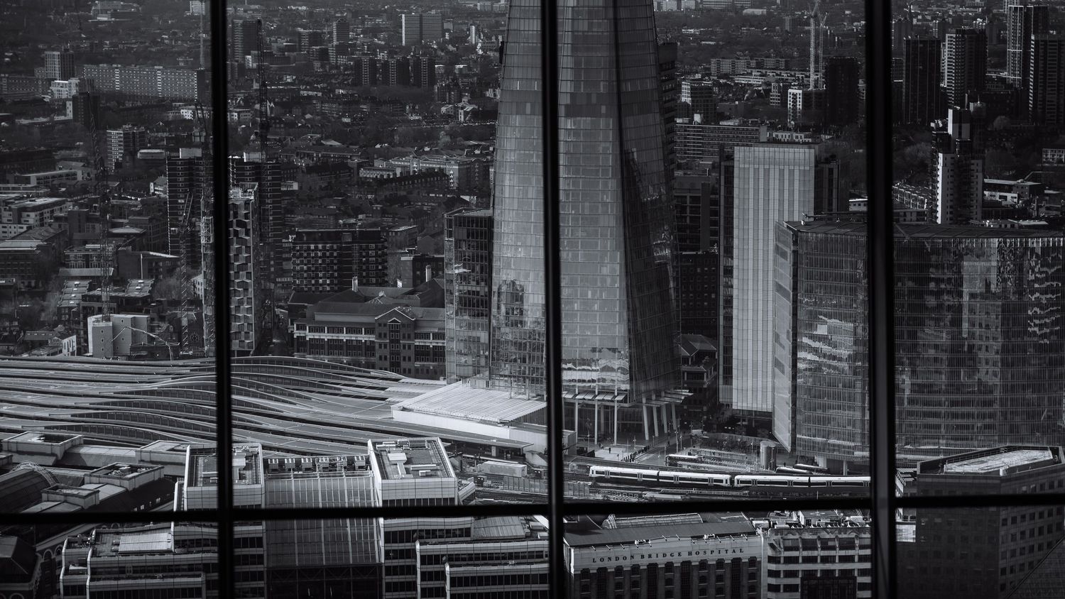 Panoramic cityscape view of modern skyscrapers and urban architecture against a gray sky.
