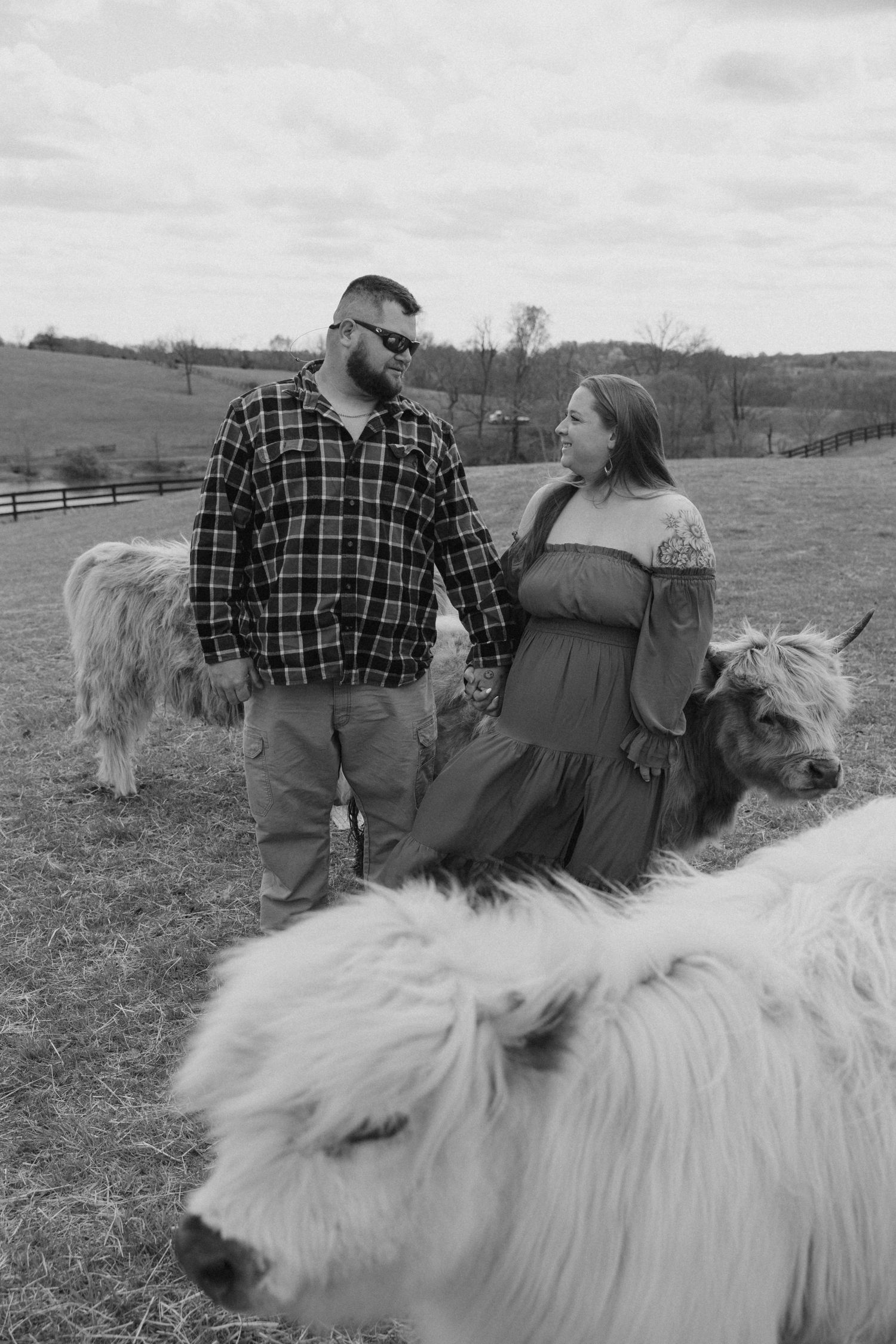 Couple sits together on fluffy white pony in rustic countryside setting.