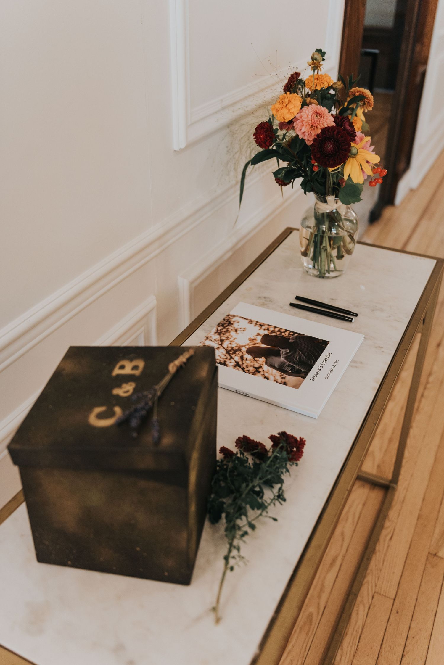 A wooden box with floral arrangements sits on a light wooden surface beside decorative elements and vases.