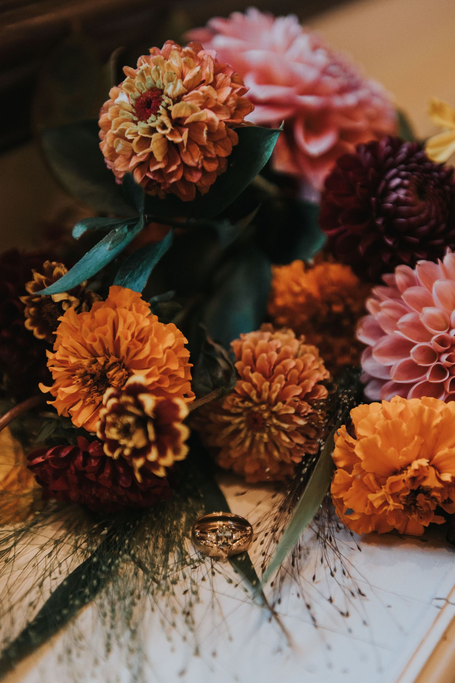 Close-up view of orange and pink dahlias with dark burgundy blooms and delicate dried flowers arranged on a light surface.