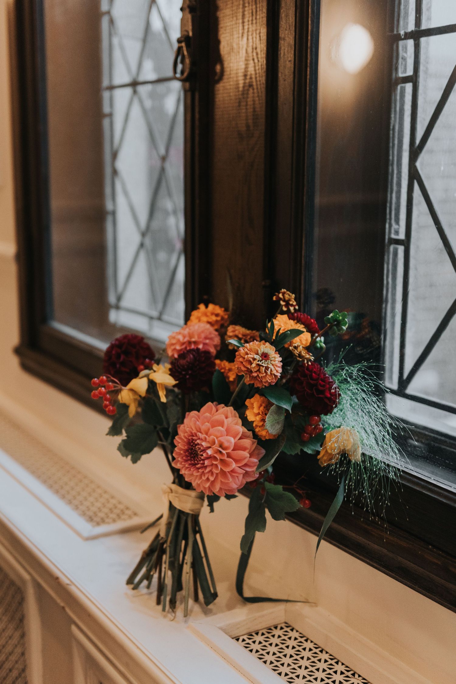 A moody autumn floral bouquet with dahlias and roses sits on a windowsill in warm natural lighting.