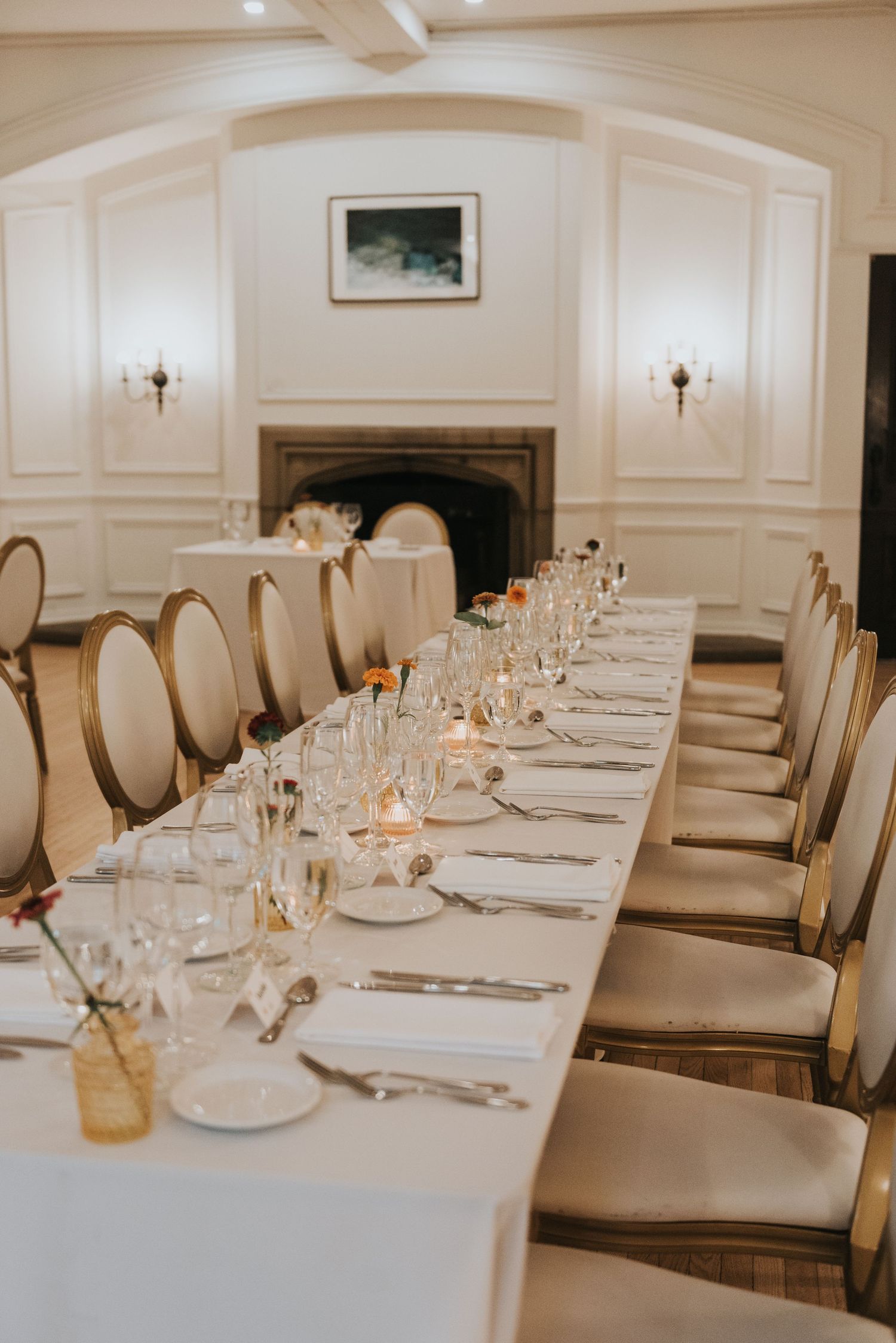 Long dining table with white tablecloth, upholstered chairs, and formal place settings in an upscale restaurant interior.