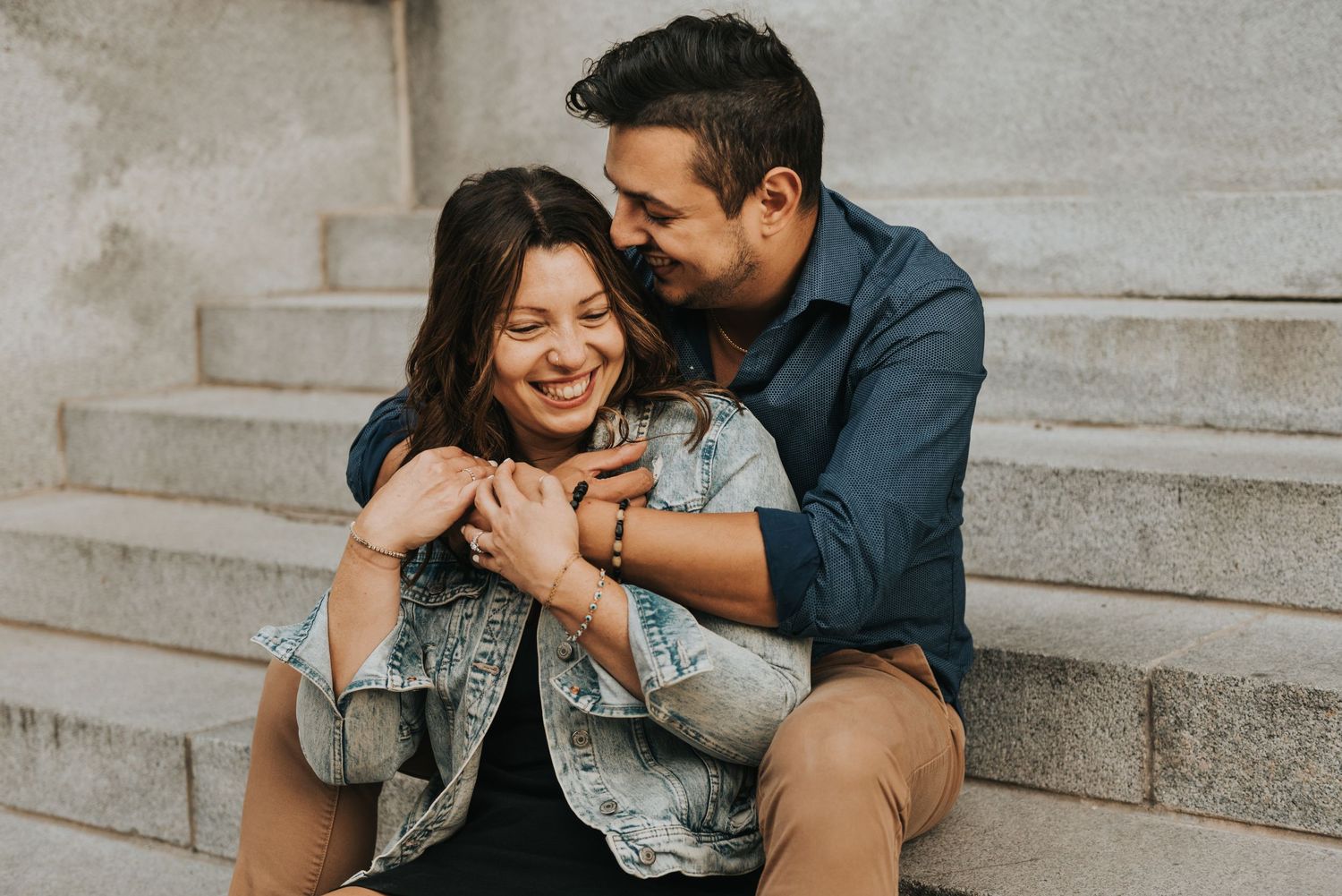 A couple shares a tender moment while sitting on concrete steps during a romantic outdoor photoshoot.