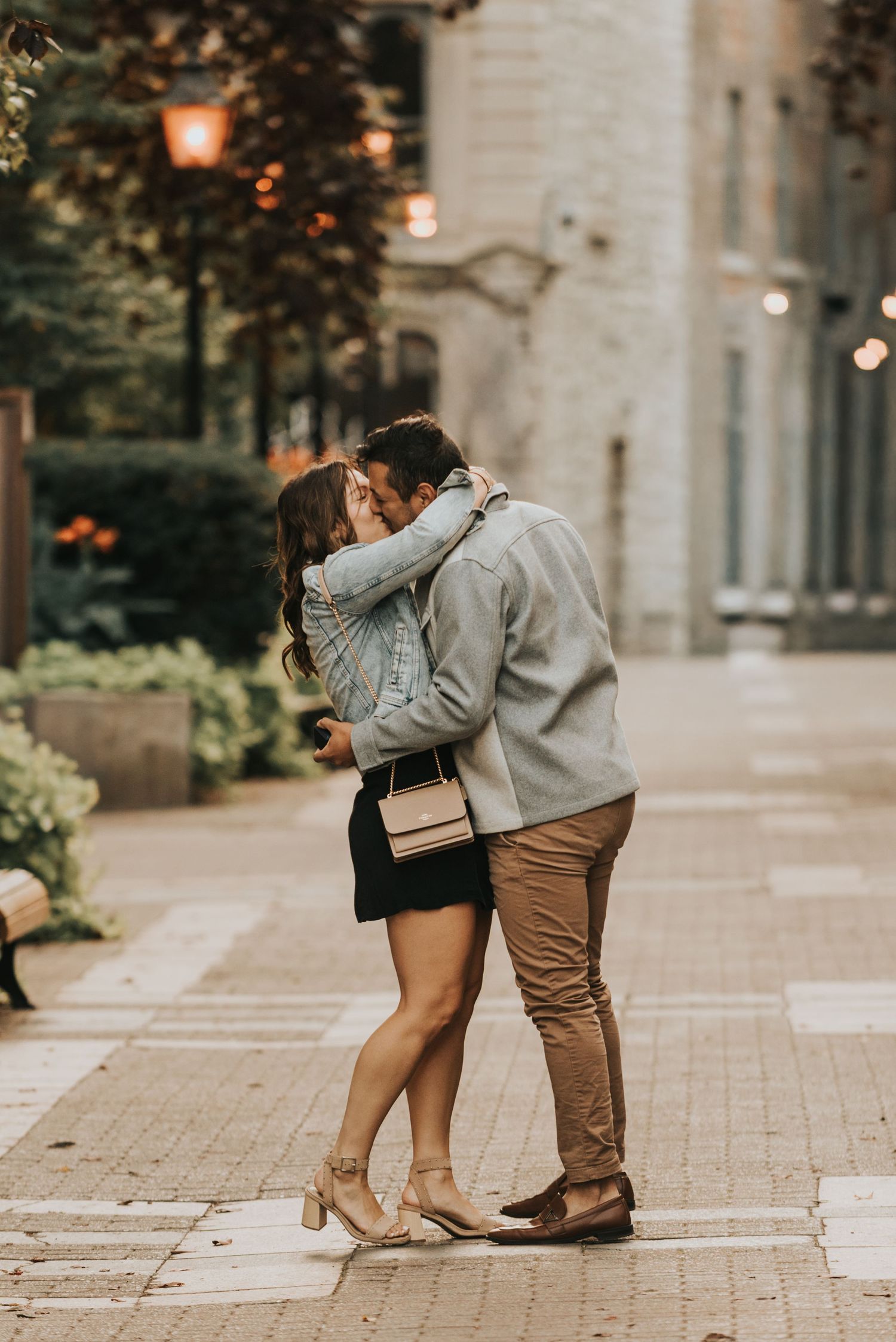A romantic couple shares an intimate moment on a cobblestone path with glowing lanterns in the evening light.