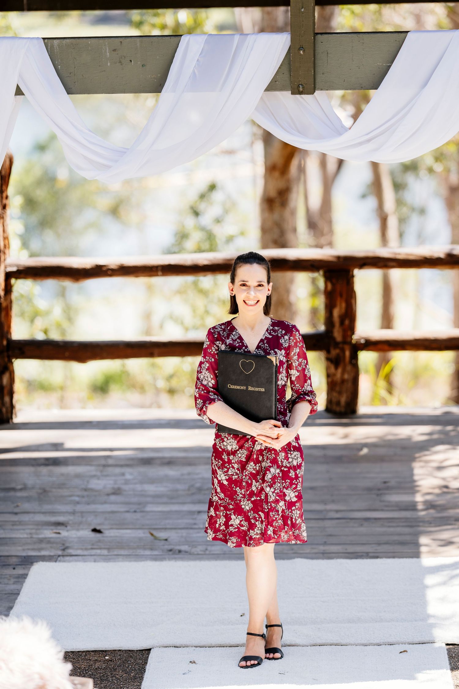 A person in a floral dress sits on a circular macrame rug in a rustic outdoor pavilion setting.