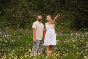 Couple enjoying a romantic moment in a wildflower meadow with evergreen forest in the background.